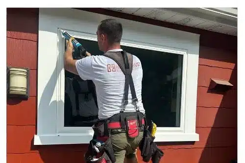 HomeTrust installer in a company shirt applying exterior sealant around a newly installed replacement window